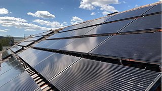 Foto, Nahaufnahme von Photovoltaik-Kollektoren auf einem Dach vor blauem Himmel.