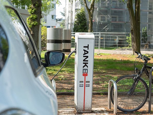 Foto, Elektroauto lädt an Ladestation neben Fahrradständer mit schwarzem Fahrrad