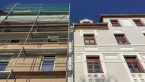 Foto, Fassaden zweier Altbauten mit Gerüst am linken Gebäude und blauem Himmel im Hintergrund