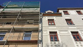 Foto, Fassaden zweier Altbauten mit Gerüst am linken Gebäude und blauem Himmel im Hintergrund