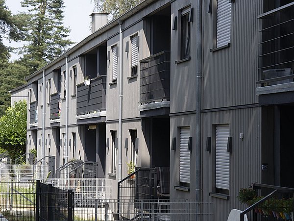 Foto, Reihe moderner Reihenhäuser mit grauer Fassade, Balkonen und kleinen Vorgärten, umgeben von Bäumen