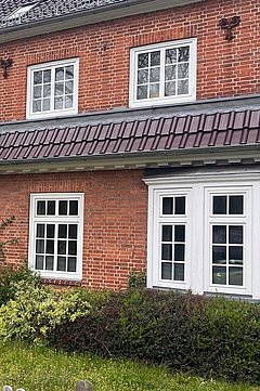 Foto, Zweistöckiges rotes Backsteingebäude mit mehreren weißen Fenstern, einem Schild mit der Aufschrift 'POLIZEI' und einem kleinen Garten mit Sträuchern davor.