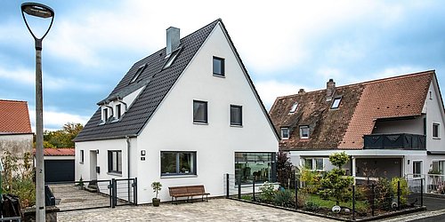Foto, Einfamilienhaus mit Einfahrt, Garten und Photovoltaikanlage nach serieller Sanierung. 