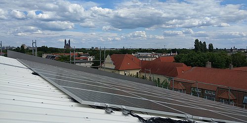 Foto, Solaranlage auf einem Dach mit Blick auf eine Stadtlandschaft und bewölktem Himmel