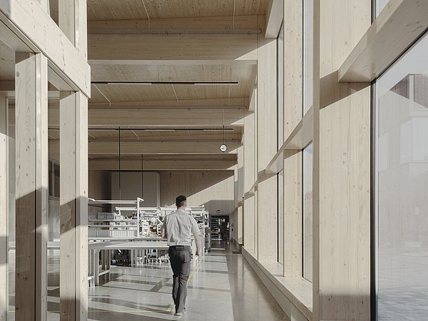 Foto, Blick in das Gebäude mit großen Fenstern, Holzbalken und einer Person, die auf eine Maschine zugeht.
