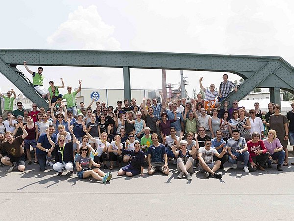 Foto, Gruppenbild einer großen Gruppe Menschen auf einer Brücke. Im Hintergrund stehen stählerne Brückenpfeiler.