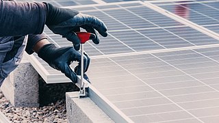 Foto, Nahaufnahme eines eines Monteurs, der ein Photovoltaikmodul auf einem Flachdach installiert.