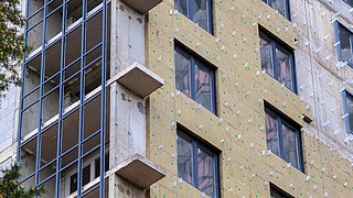 Foto, Blick hinauf an der Fassade eines Mehrfamilienhauses, an dem Dämmung angebracht wird