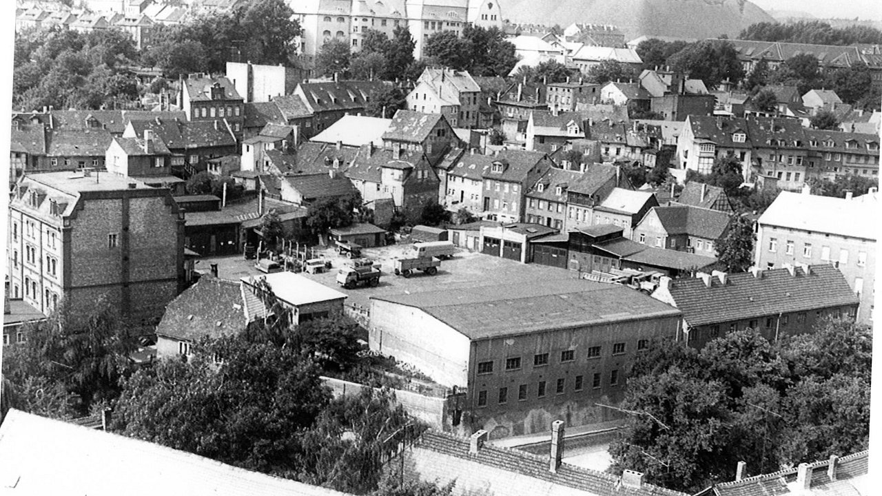 Foto, Historische Luftaufnahme eines Stadtteils mit dicht stehenden Gebäuden und Fabrikgebäuden, umgeben von Bäumen