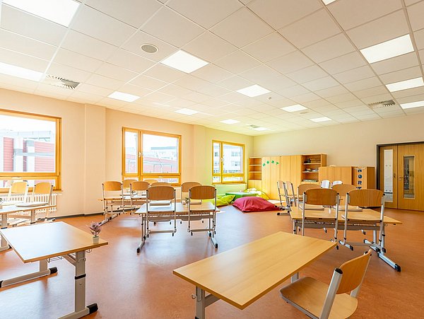 Foto, Klassenzimmer mit Tischen, die im Raum verteilt angeordnet sind. Im Hintergrund befindet sich eine Sitzecke mit Sitzsäcken.