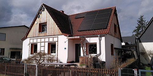 Foto, Einfamilienhaus mit teilweiser Holzverkleidung an der Fassade und Photovoltaikanlage auf dem Dach. 