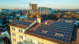 Foto, Blick von oben auf dem Dach eines Mehrfamilienhauses mit Photovoltaikanlage. Im Hintergrund Baustelle eines Hochhauses mit Kränen.