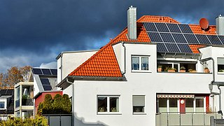 Foto, mehrere Häuser versetzt hintereinander mit Solaranlagen auf dem Dach.