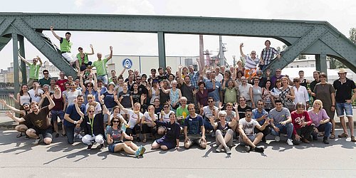Foto, Gruppenbild einer großen Gruppe Menschen auf einer Brücke. Im Hintergrund stehen stählerne Brückenpfeiler.