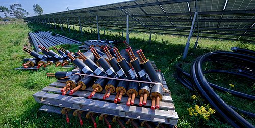 Foto, Isolierte Rohre mit Kupferleitungen auf Holzpaletten neben einer großen Solaranlage im Freien