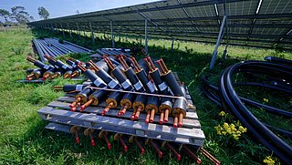 Foto, Isolierte Rohre mit Kupferleitungen auf Holzpaletten neben einer großen Solaranlage im Freien