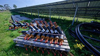 Foto, Isolierte Rohre mit Kupferleitungen auf Holzpaletten neben einer großen Solaranlage im Freien