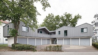 Foto, Moderne Wohngebäude mit grauen Fassaden und Garagen im Erdgeschoss, umgeben von Bäumen und Gehweg