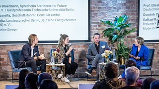 Foto, Vier Personen sitzen auf einer Bühne vor Publikum, diskutieren bei der Jahrestagung 2024, im Hintergrund Text mit Namen und Titeln der Panelteilnehmer