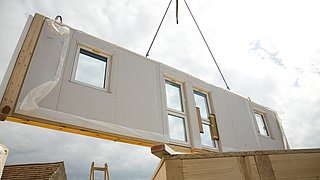 Foto, ein vorgefertigetes Bauelement für ein modulares Gebäude hängt an einem Kran.