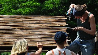 Foto, drei Frauen montieren Bambus-Stäbe auf einer Holzkonstruktion.