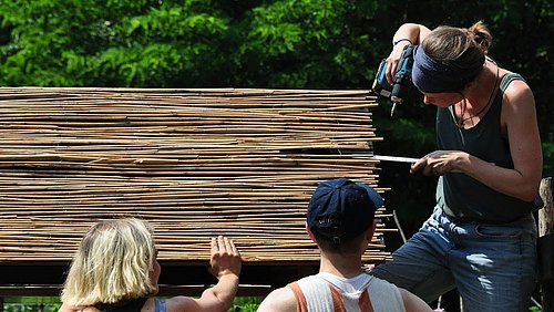 Foto, drei Frauen montieren Bambus-Stäbe auf einer Holzkonstruktion.