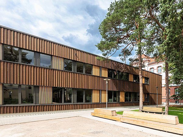 Foto, Außenansicht von Gebäude mit Holzfassade und Fensterreihen über die gesamte Länge.