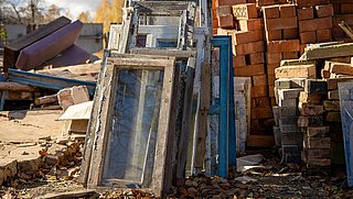 Foto, im Vordergund ein großer Stapel alter Ziegelsteine, daran angelehnt mehere alte Fensterelemente. Im Hintergrund weitere Bauabfälle.