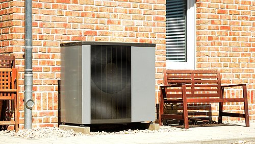 Foto, Wärmepumpe und Gartenbank vor einem Haus.