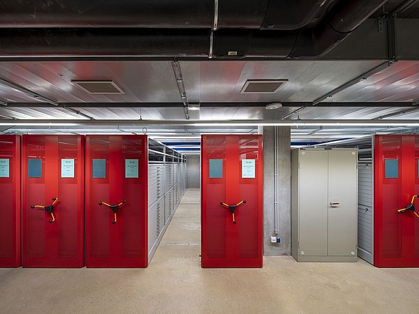 Foto, eine riehe von Magazinen in einem Archiv mit roten Fronten und Kurbeln.