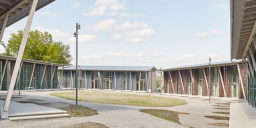 Foto, Moderne Wohnsiedlung mit flachen, langgestreckten Gebäuden und großen Fenstern, umgeben von Wegen und Rasenflächen