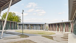 Foto, Moderne Wohnsiedlung mit flachen, langgestreckten Gebäuden und großen Fenstern, umgeben von Wegen und Rasenflächen