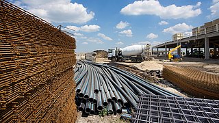 Foto, gelagerte Baustoffe und -materialien auf einer Baustelle, im Hintergrund ein Betonmischer.