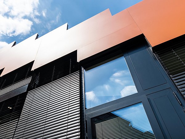 Foto, Fassade eines modernen Gebäudes mit schwarzen Lamellen und orangefarbenen Paneelen unter blauem Himmel