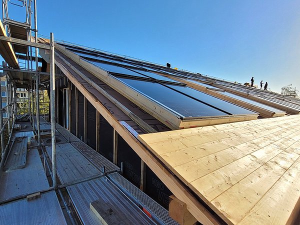 Dach mit montierten Solarpaneelen und Holzverkleidung, umgeben von Gerüst, bei klarem Himmel.