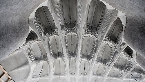 Foto, Blick nach oben auf eine Geschossdecke aus einer Leichtbau-Betonplatte mit außergewöhnlich komplexer Form, die mittels 3D-gedruckter Schalung hergestellt wurde.