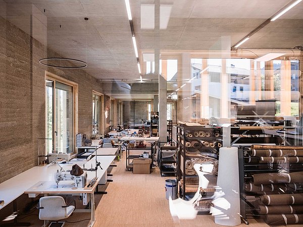 Foto, heller, moderner Arbeitsraum mit Nähmaschinen, Stoffrollen und großen Fenstern