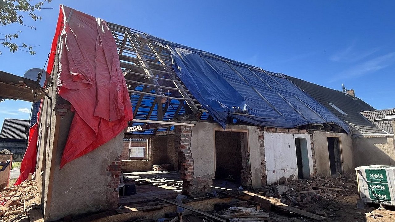 Foto, Haus während Sanierung, Haus mit teilweise entferntem Dach, das mit blauer und roter Plane abgedeckt ist