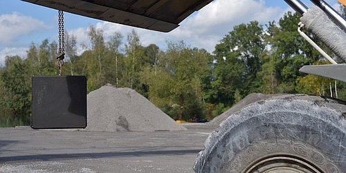 Foto, eine Testquader aus Klimabeton hängt an einer Baggerschaufel.