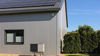 Foto, Seitenansicht eines modernes Einfamilienhaus mit einer Solaranlage auf dem Dach und eine davor aufgestellten Wärmepumpe.