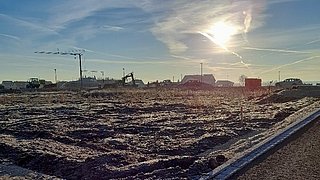 Foto, Panoramabild einer Baustelle. In der Ferne stehen Kräne vor einem blauen Himmel.