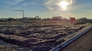 Foto, Panoramabild einer Baustelle. In der Ferne stehen Kräne vor einem blauen Himmel.