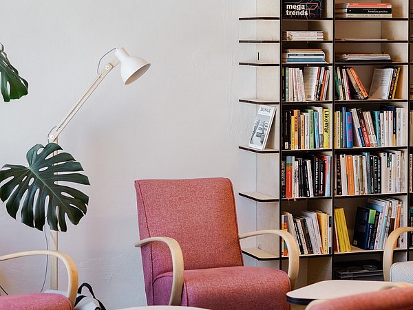 Zwei rot gepolsterte Sessel mit hellen Holzarmlehnen vor einem Bücherregal mit vielen Büchern und einer weißen Stehlampe mit verstellbarem Arm.