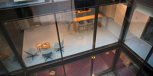 Foto, Aufnahme durch eine Scheibe in den Innenraum mit Holztisch und Barstühlen