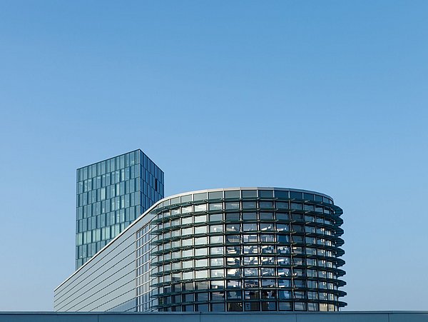 Foto, der obere Teil eines halbrunden Gebäudes steht vor einem Hochhaus mit Glasfassade