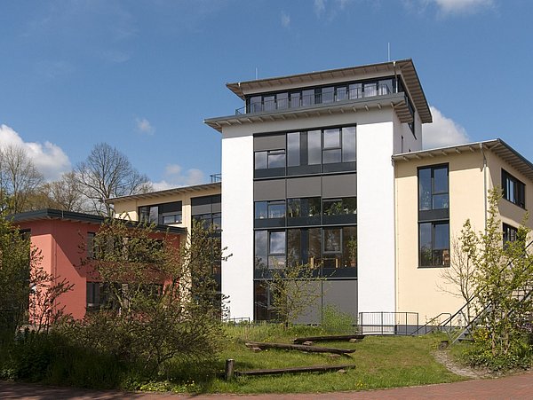 Foto, Außenaufnahme eines kleinen, mehrstöckigen und modernen Gebäudes.