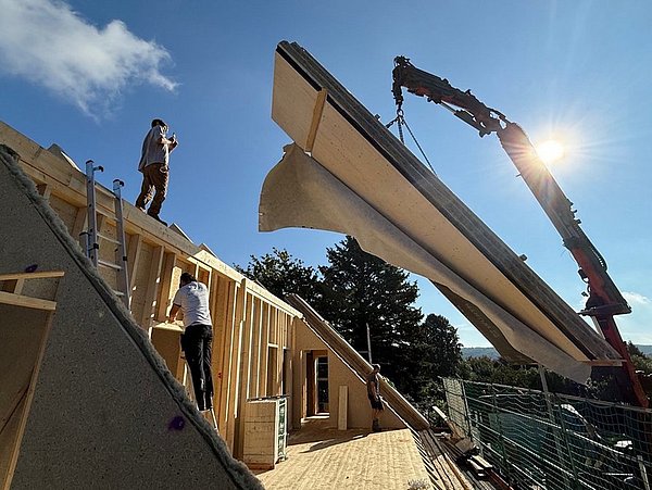 Foto, Blauer Himmel mit Haus, Dachstuhl im Ausbau, ein Fassadenelement wird mit dem Krank angeliefert