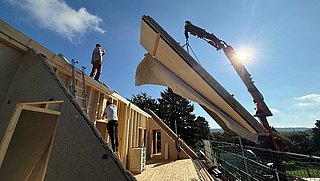 Foto, Blauer Himmel mit Haus, Dachstuhl im Ausbau, ein Fassadenelement wird mit dem Krank angeliefert