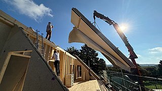 Foto, Blauer Himmel mit Haus, Dachstuhl im Ausbau, ein Fassadenelement wird mit dem Krank angeliefert