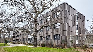 Foto, saniertes Verwaltungsgebäude mit grauer Holzfassade.